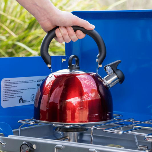 Red kettle being used on a camping stove with a blue background