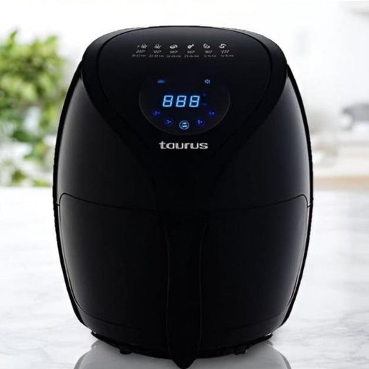 Black Taurus digital air fryer with timer on a white surface with blurred greenery in the background
