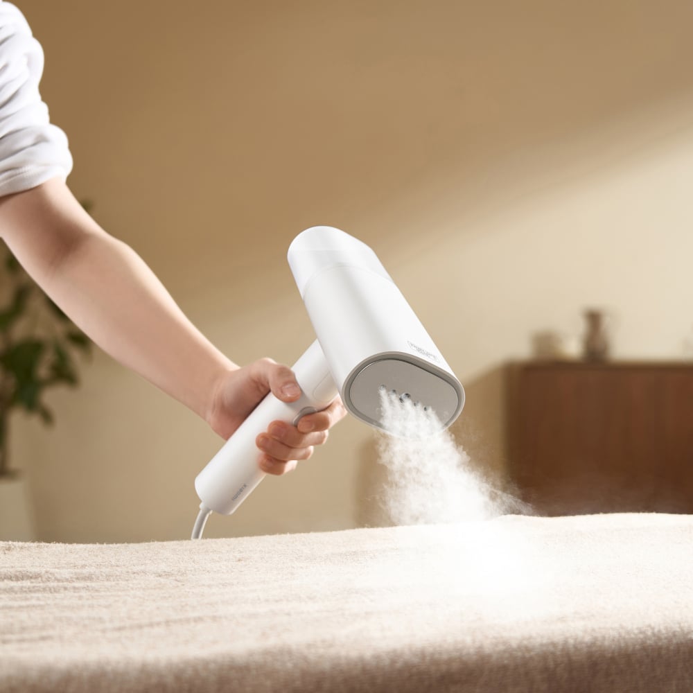 Person using a handheld steamer on a bed in a bedroom setting