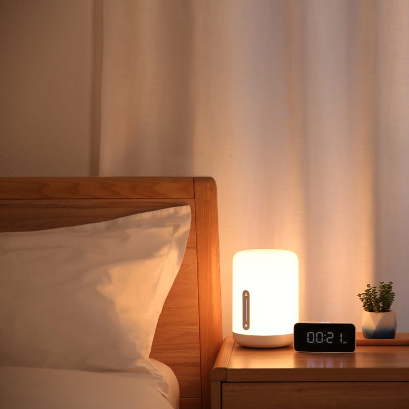 Bedroom scene with a nightstand lamp and clock on a wooden bedside table.