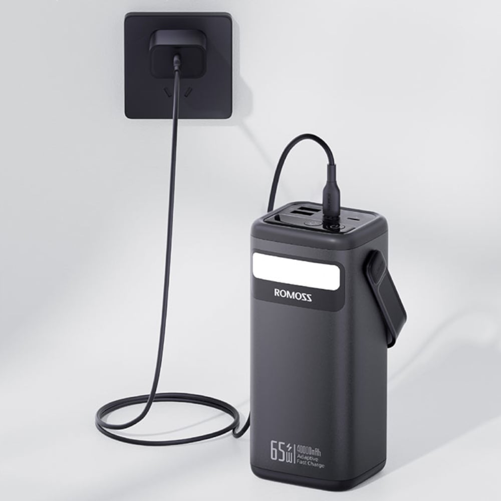Black power bank with USB cable attached to a wall socket on a light gray background