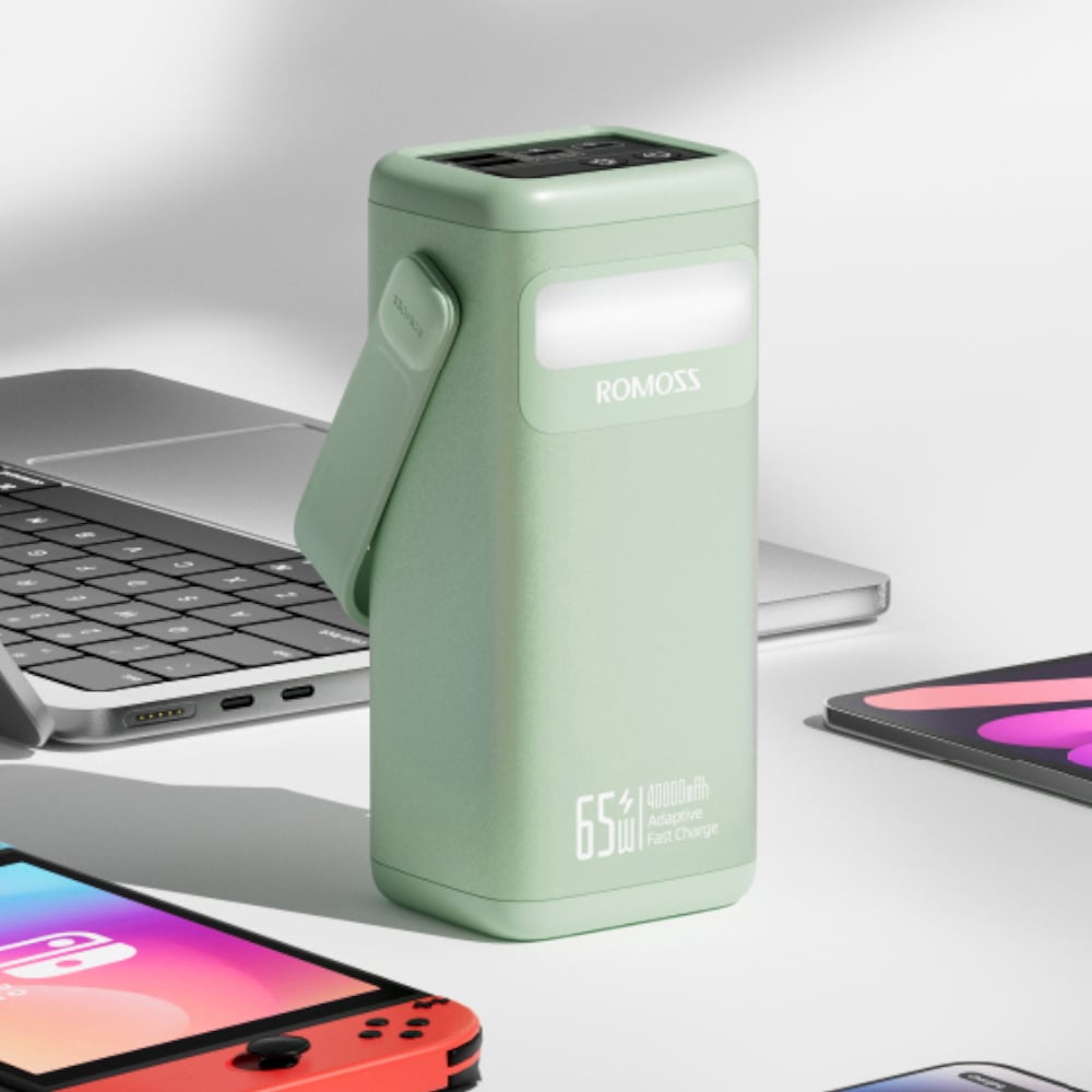 Green power bank with 'ROMOSS' branding on a desk with electronic devices.