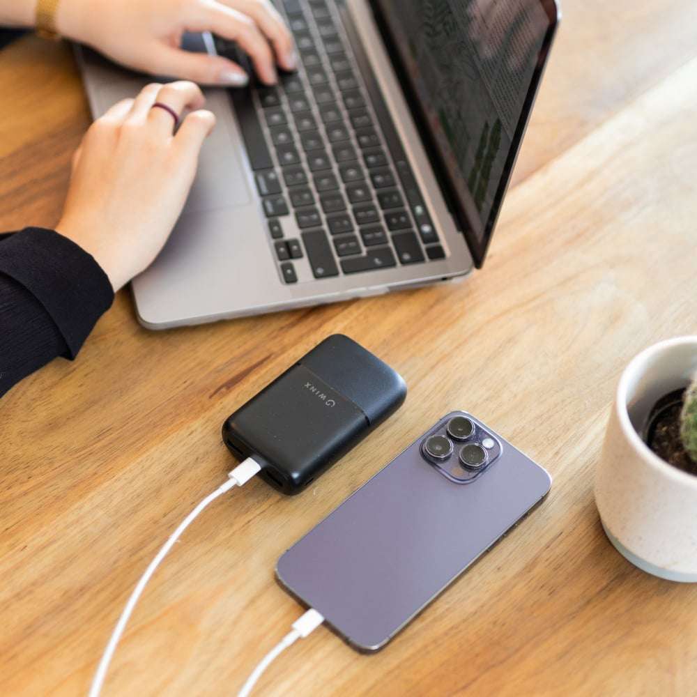 Person using a laptop with a smartphone and power bank on a wooden desk