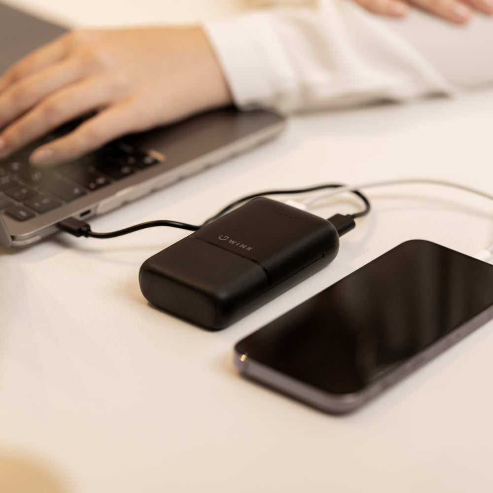 Black USB drive connected to a smartphone on a desk with a blurred laptop in the background.