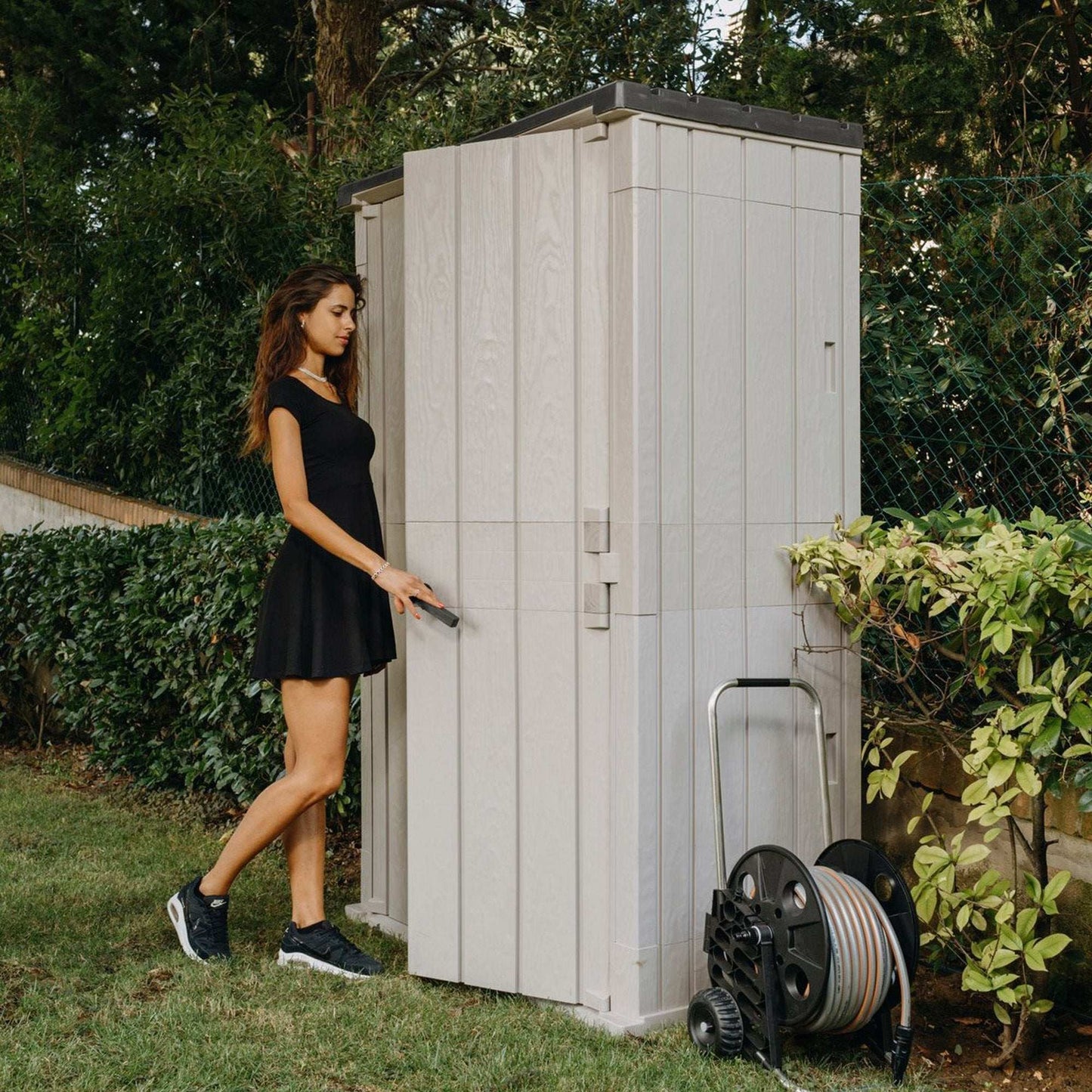 Woman opening a storage shed in a garden setting