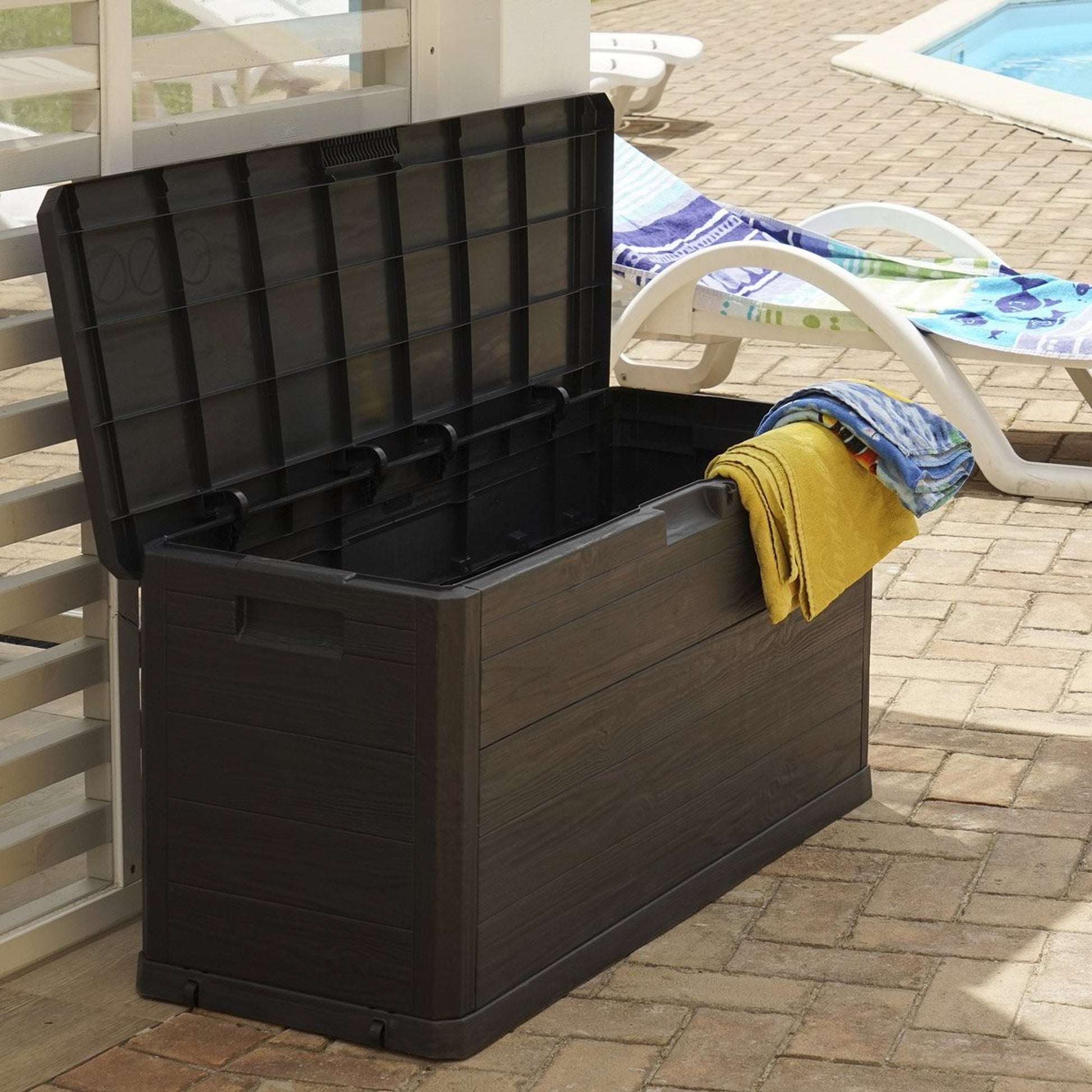Black storage box with towels on a patio near a pool