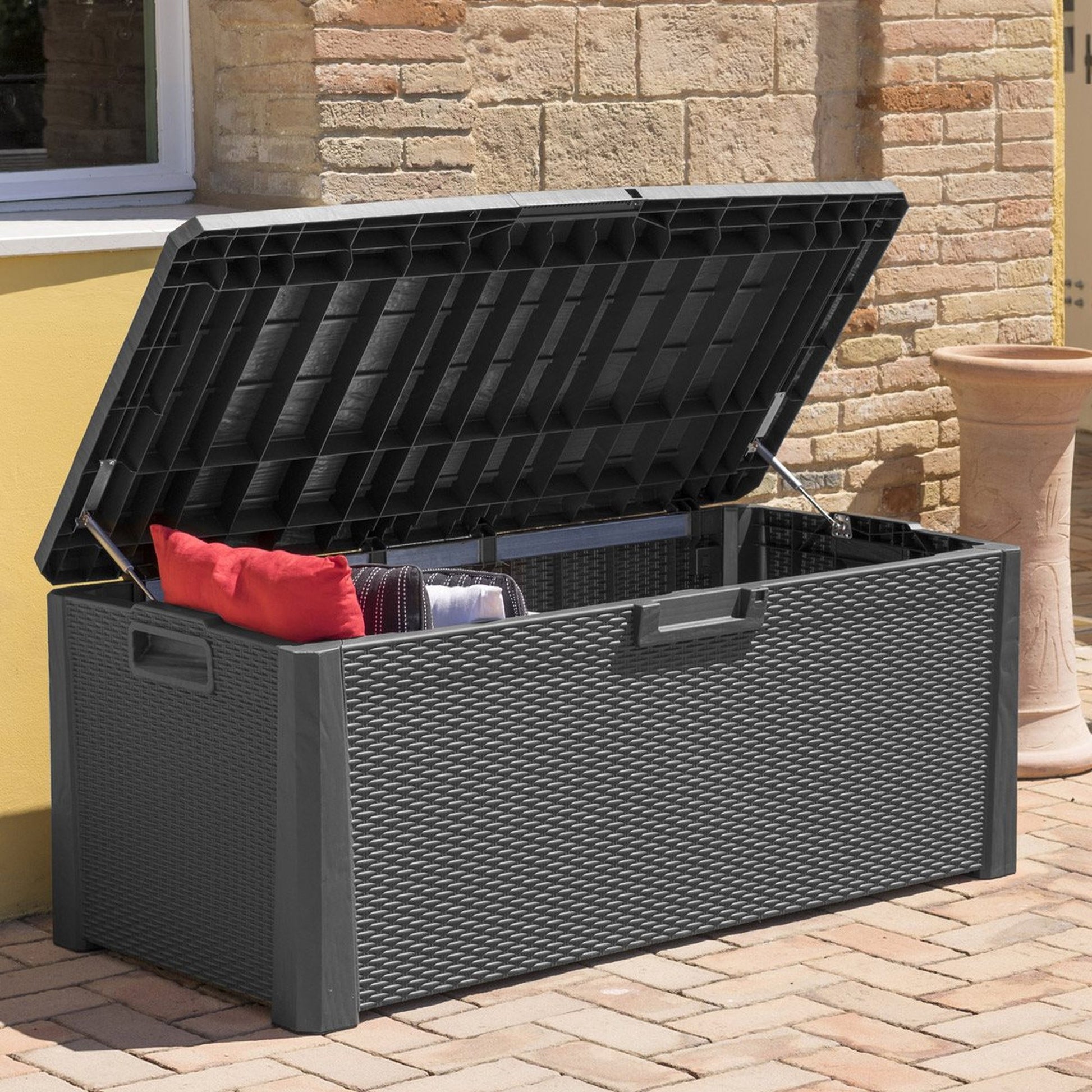 Outdoor storage bench with a black lid and red pillow on a patio.