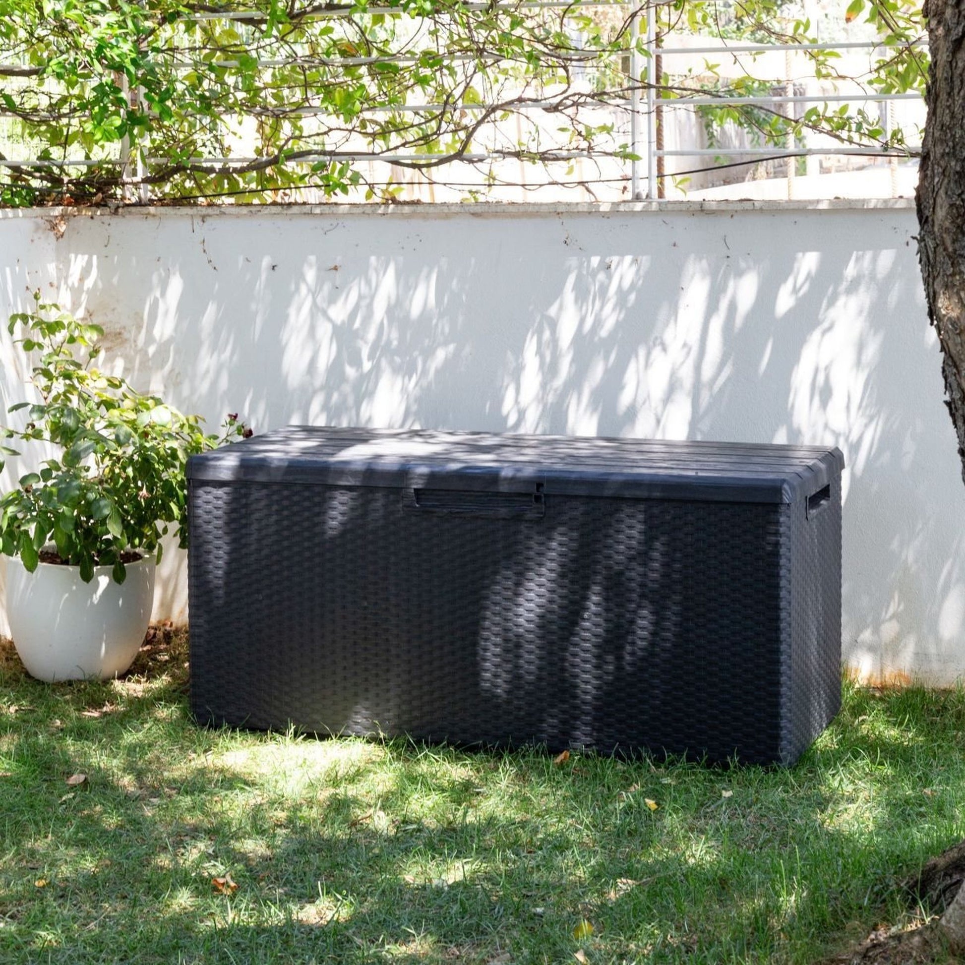 Black outdoor storage box on grass with a white wall and tree in the background