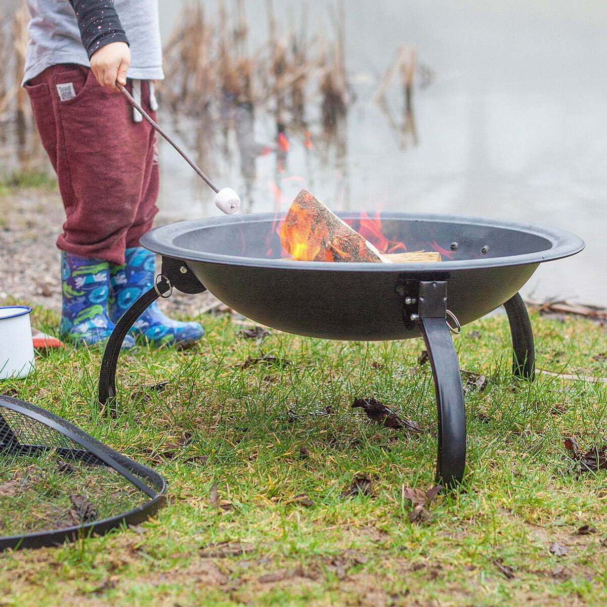 Person roasting marshmallows over a fire pit by a lake