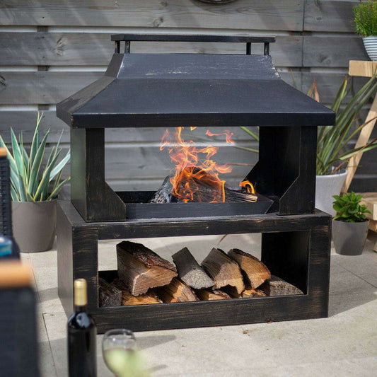 Outdoor fireplace with fire burning and wood logs in a garden setting.