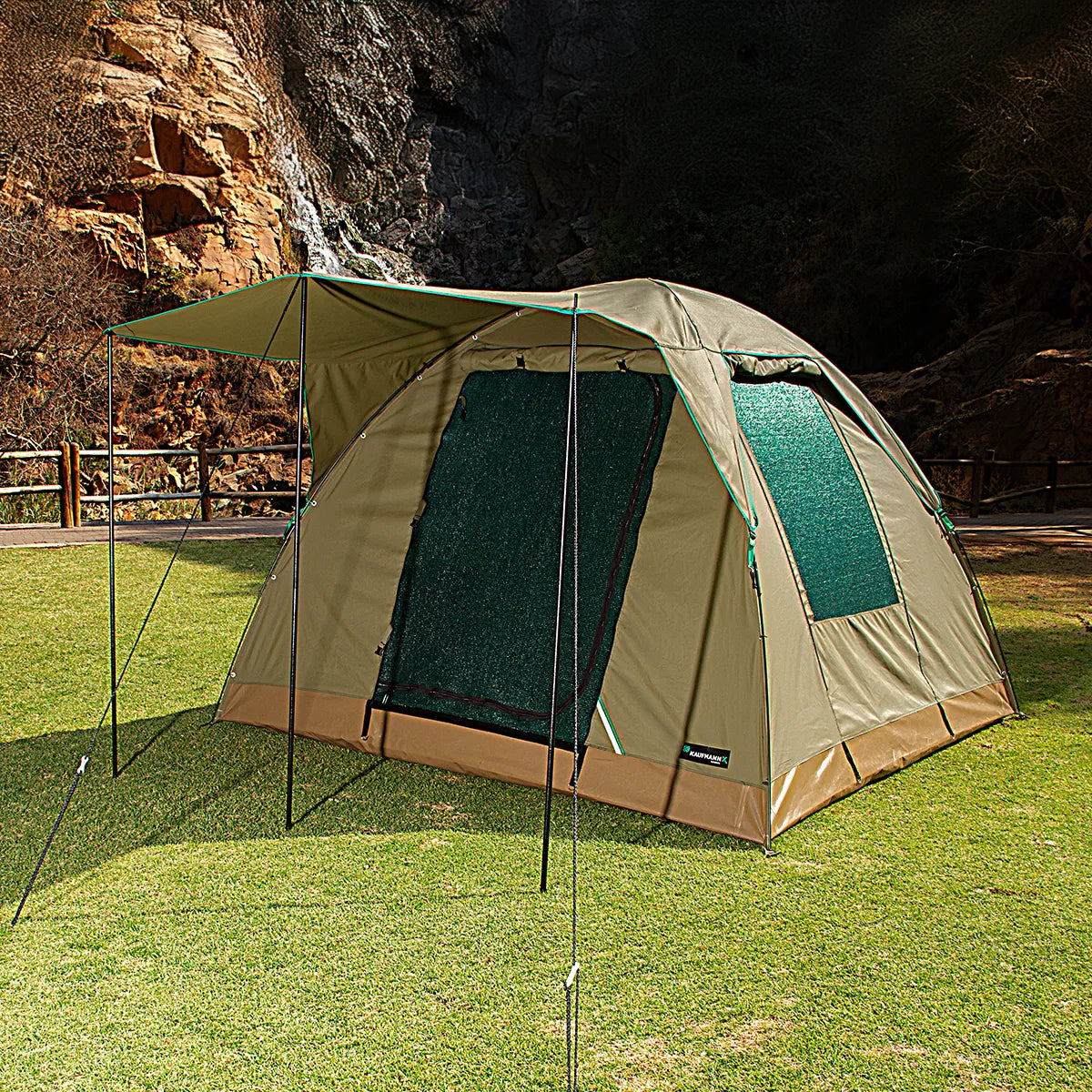 Camping tent with attached screen porch on grassy area with rocky cliff background