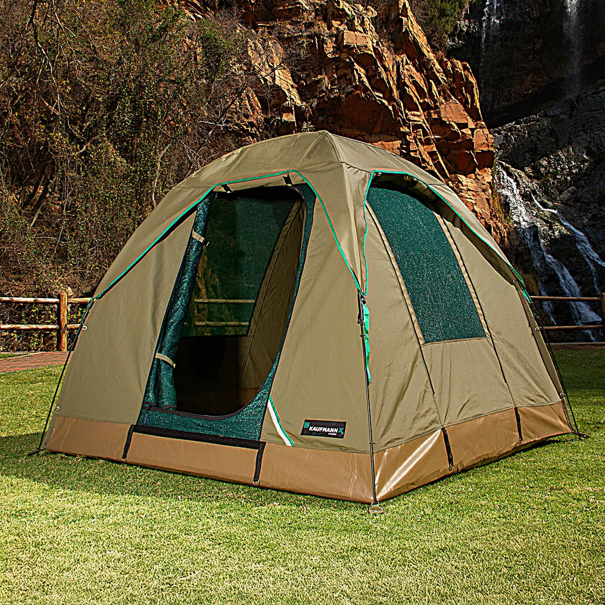 Green and brown tent set up outdoors with a waterfall in the background