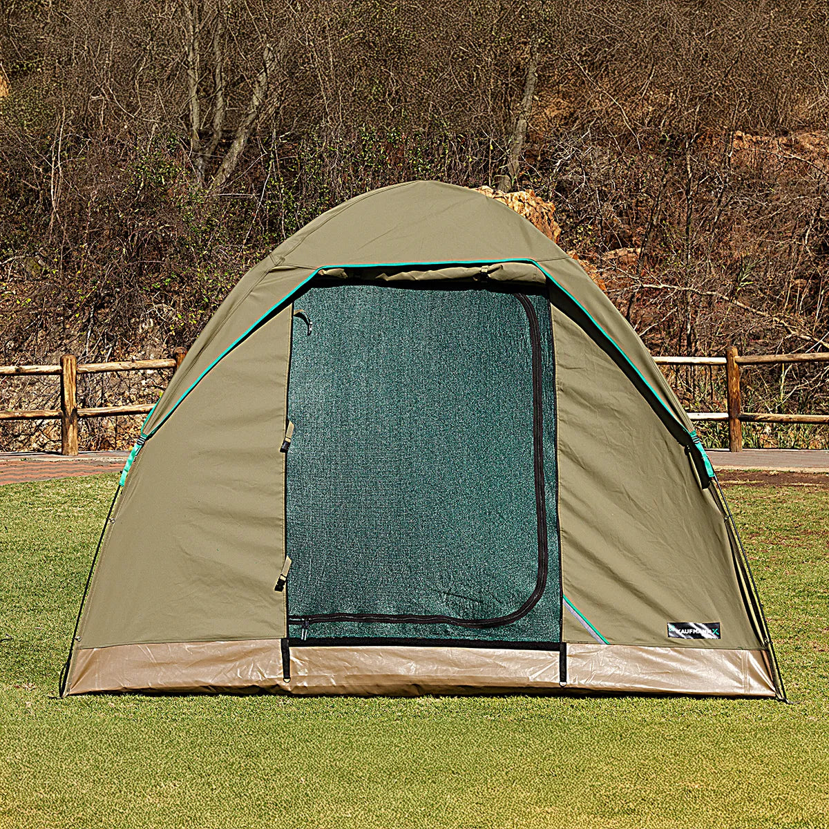 Green camping tent with a mesh door on a grassy area with trees in the background
