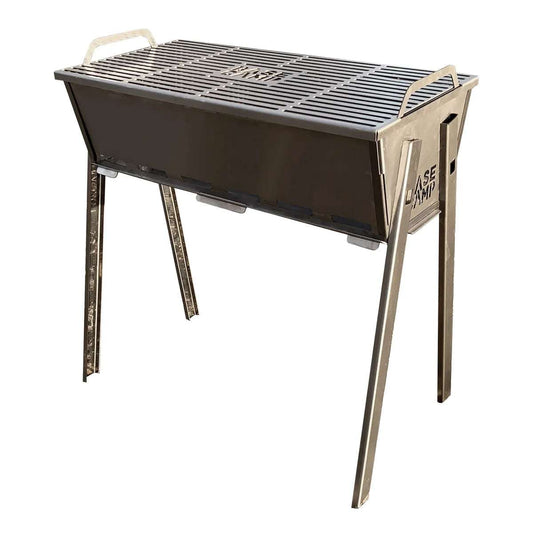 A stainless steel Basecamp Eco Braai grill with folding legs and a closed lid, placed on a flat surface.