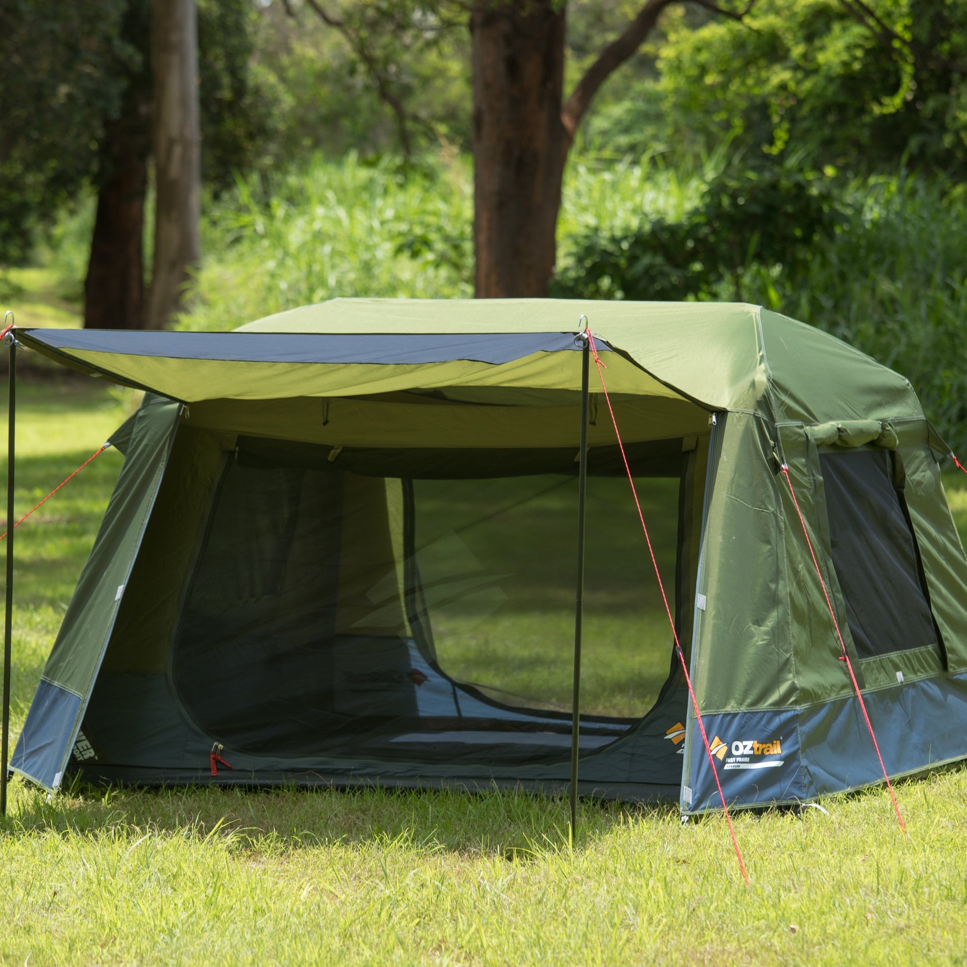 Green camping tent with a screen porch in a grassy area with trees