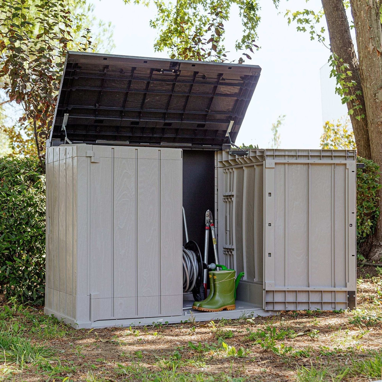 Outdoor storage shed with tools and equipment inside, surrounded by trees and greenery.