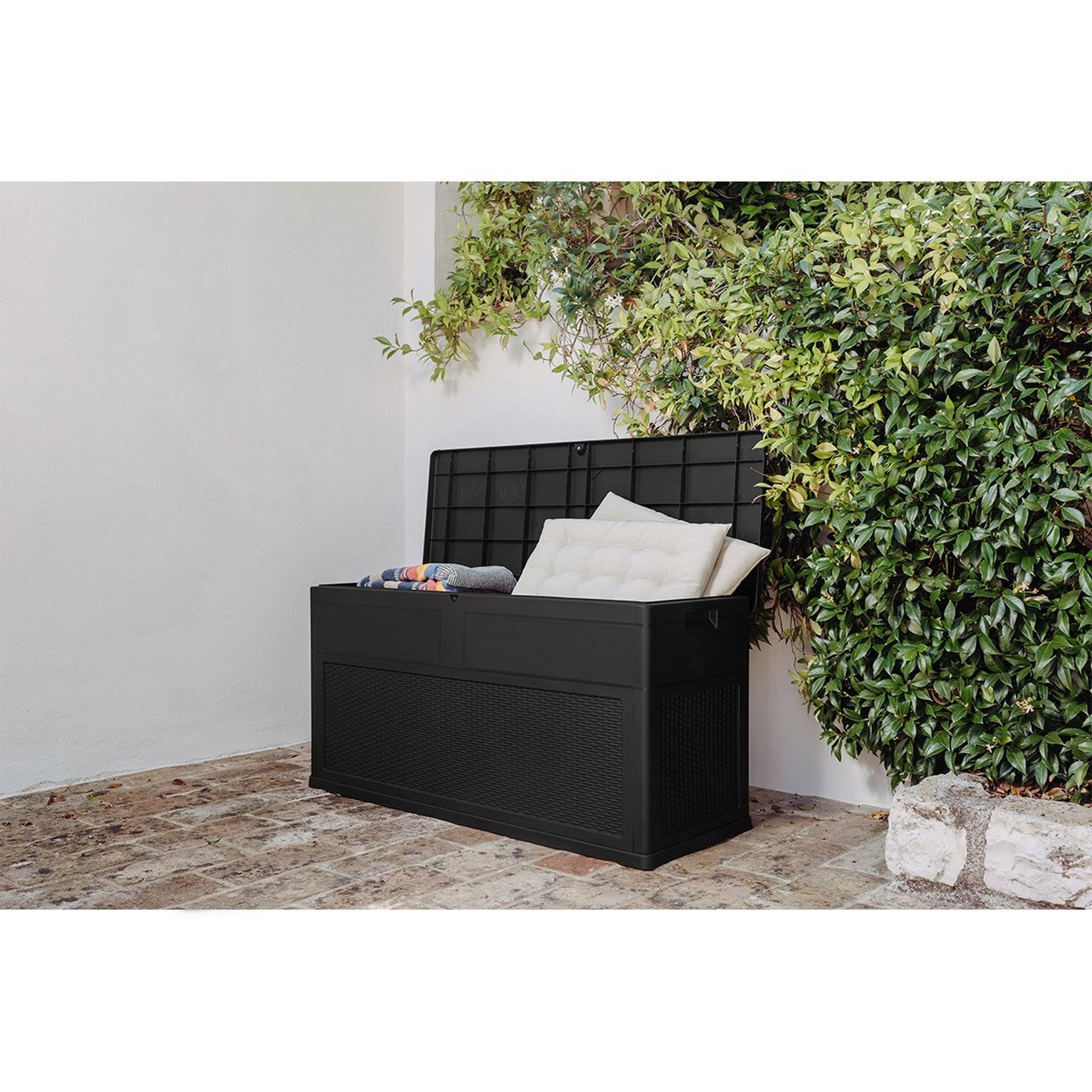 Black storage bench with cushions against a white wall with greenery
