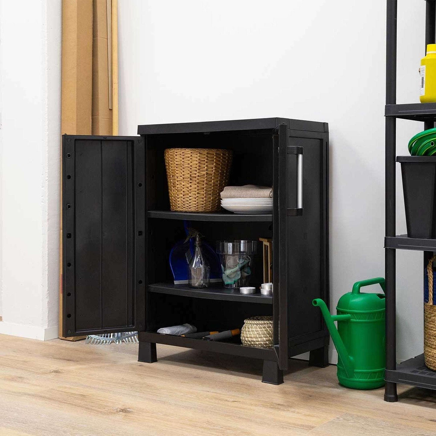 Black storage cabinet with open door on a wooden floor, containing various items.