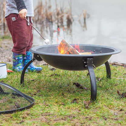 Person roasting marshmallows over a fire pit by a lake