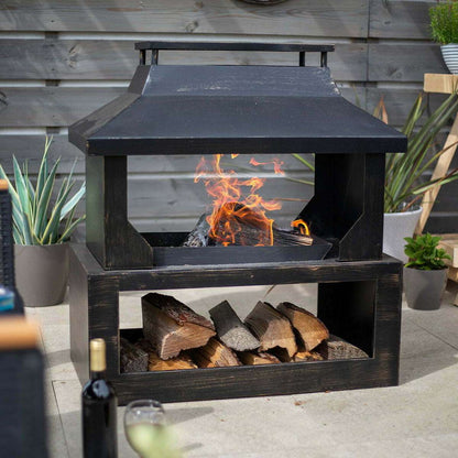 Outdoor fireplace with fire burning and wood logs in a garden setting.